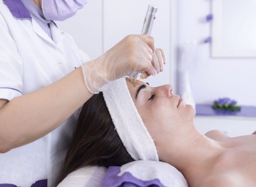 close up of Cosmetologist,beautician applying facial dermapen treatment on face of young woman customer in beauty salon.Cosmetology and professional skin care, face rejuvenation.