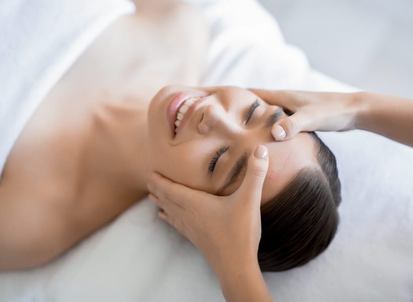 Masseuse keeping her hands on forehead of young client during massage of face