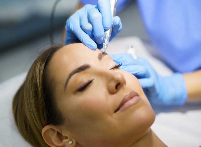 Permanent make-up for eyebrows of beautiful woman in a beauty salon. Close-up of beautician doing tattooing eyebrow. Micropigmentation treatment.